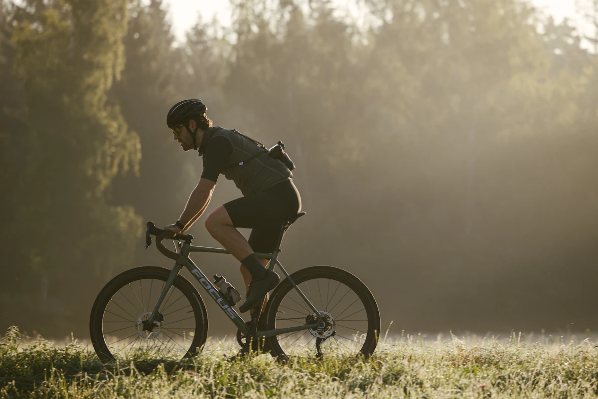 A cyclist on a gravel bike rides through a grassy clearing in low golden light.