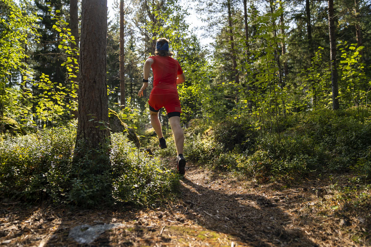 A runner in red on a sunlit forest trail.