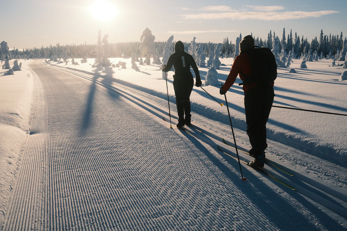 Two cross-country skiers on a groomed trail in low winter sun.